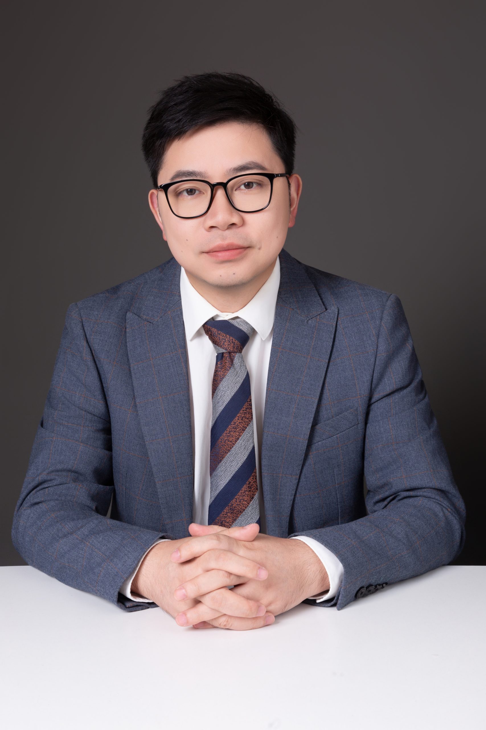 Portrait of Pascal Yin in a grey checked suit, hands folded